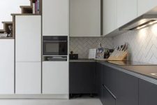 a modern graphite grey and white kitchen with sleek cabinets, a herringbone tile backsplash and built-in lights