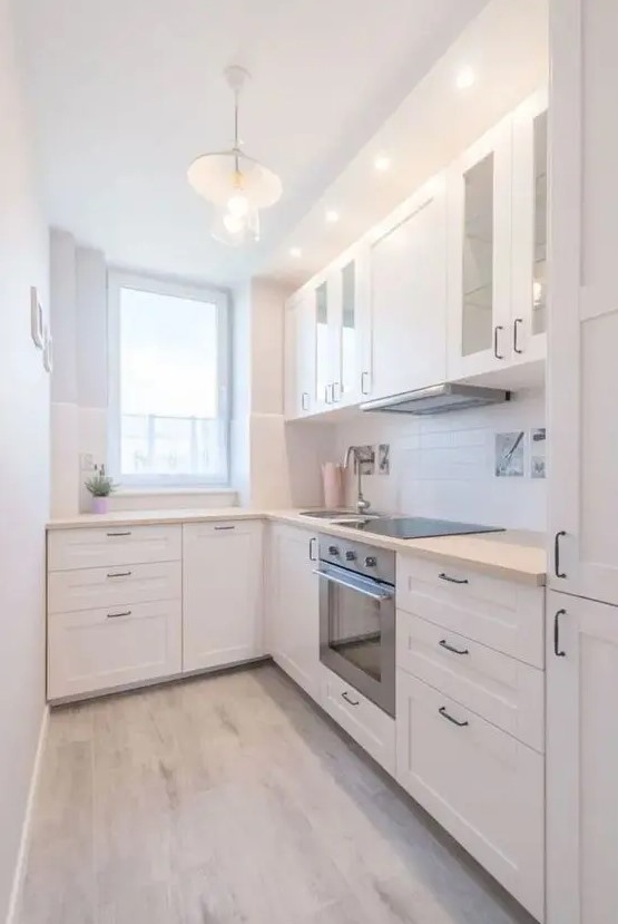 A modern white L shaped kitchen with a white tile backsplash and light stained butcherblock countertops