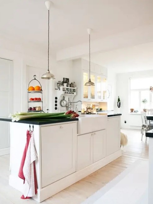 a modern white Scandinavian kitchen with a large kitchen island with a black countertop, pendant lamps and a glass buffet