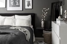 a monochromatic bedroom with black walls, a black upholstered bed, monochromatic bedding and a white dresser