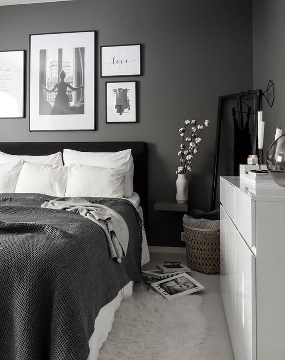 a monochromatic bedroom with black walls, a black upholstered bed, monochromatic bedding and a white dresser