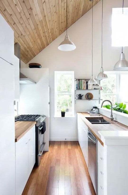 a narrow attic kitchen with white cabinets, butcherblock countertops, pendant lamps and built in appliances