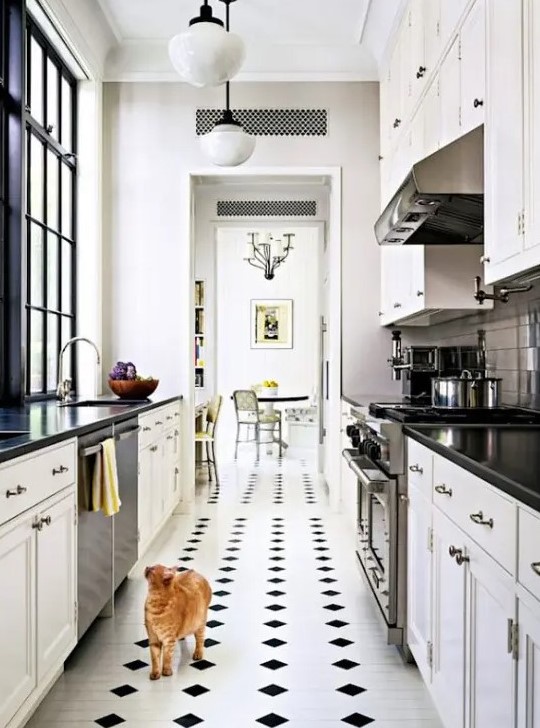 a narrow kitchen with white shaker style cabinets, black countertops, a checked floor and some pendant lamps