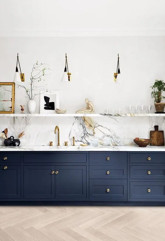 A navy one wall kitchen with a white stone backsplash and countertops, a stone shelf and sconces is super chic.