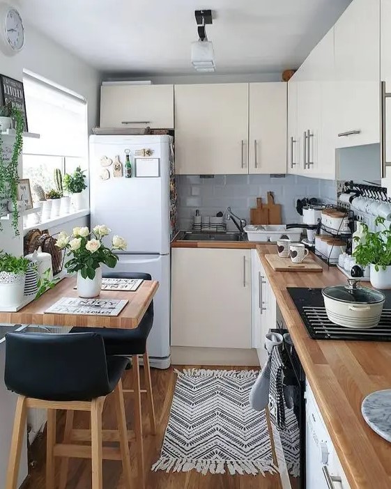 A neutral L shaped kitchen with grey tiles, butcherblock countertops and potted greenery and blooms