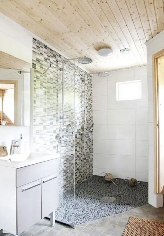 A neutral Nordic bathroom with a wooden ceiling, a mosaic tile wall and a pebble floor and an off white vanity