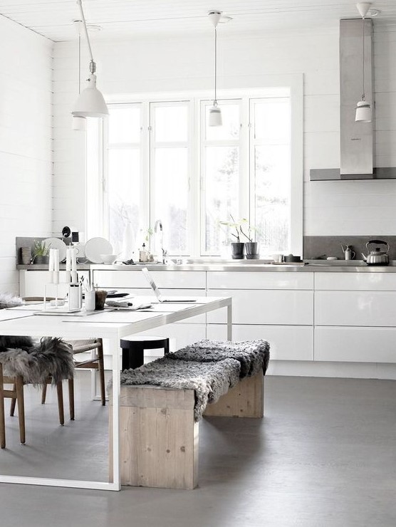 a neutral Nordic kitchen with sleke white cabinets, metal countertops, a white table and wooden benches plus pendant lamps