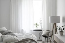 a neutral Scandi bedroom with neutral furniture, neutral bedding, a black chair with a pillow and a floor lamp