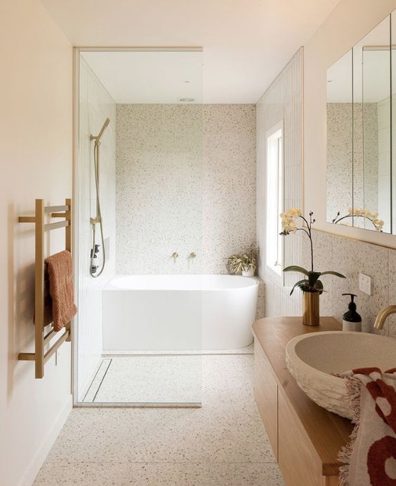 a neutral Scandinavian bathroom clad with terrazzo, with a stained vnaity and a stone sink and a shower and bathtub space