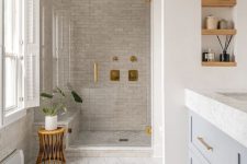 a neutral Scandinavian bathroom with marble and neutral tiles, a grey vanity, shelves, a stool and a bathtub