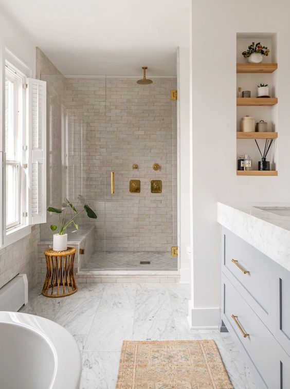 a neutral Scandinavian bathroom with marble and neutral tiles, a grey vanity, shelves, a stool and a bathtub