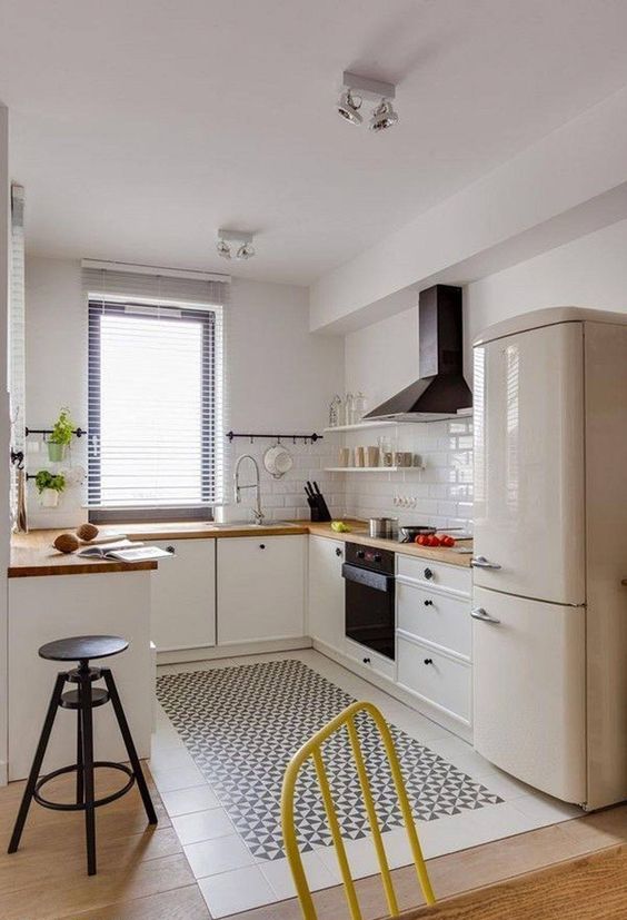 a neutral U-shaped kitchen with butcherblock countertops, black appliances, a black stool and some potted herbs