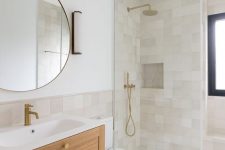 a neutral and airy Scandinavian bathroom with neutral tiles, a stained vanity, a shower space, a round mirror and brass fixtures
