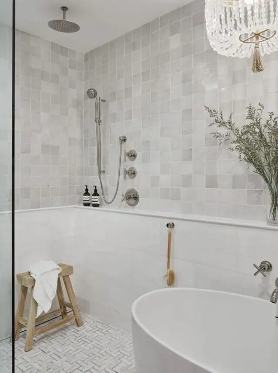 a neutral bathroom clad with zellige tiles and geo ones on the floor, an oval tub and a shower, some greenery