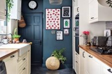 a neutral kitchen with navy walls, a pendant lamp, potted greenery, wooden countertops and a bright gallery wall
