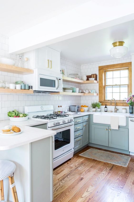 a pale blue U-shaped kitchen with shaker cabinets, open shelves, a white square tile backsplash and some blooms