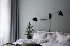 a peaceful Scandinavian bedroom infused with color, with a green accent wall, a bed with neutral bedding, mauve curtains and a black lamp