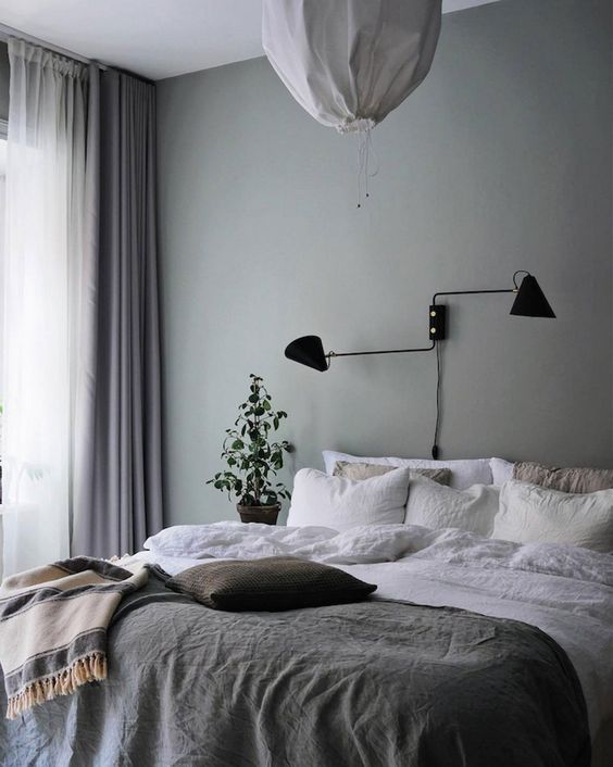 a peaceful Scandinavian bedroom infused with color, with a green accent wall, a bed with neutral bedding, mauve curtains and a black lamp