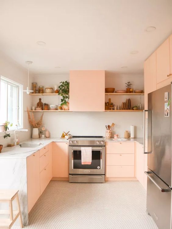 a peachy pink kitchen with open shelves, stone countertops, greenery and built-in appliances