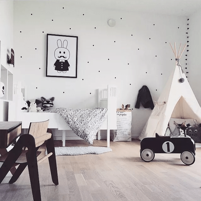 a plyaful Scandinavian kids' room in black and white, with contemporary furniture, a teepee, a polka dot wall and cool black and white toys