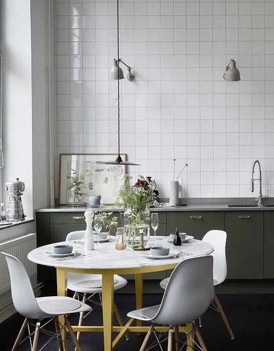 a pretty Nordic kitchen with dark green lower cabinets, white square tiles, a round table and white chairs and grey lamps
