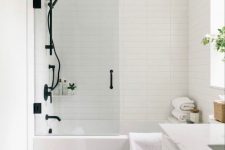 a pretty Scandinavian bathroom with skinny tiles, a white vanity, black fixtures, a basket, white towels