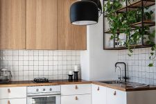 a pretty Scandinavian kitchen with white and stained cabinets, white square tiles, a stained table, black chairs and black pendant lamps