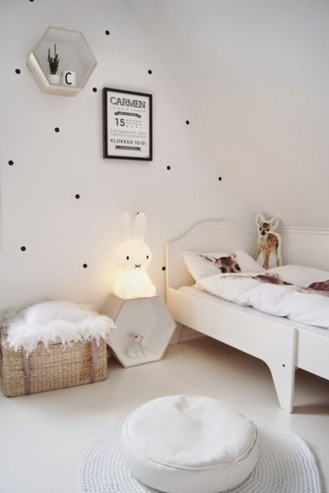 a pretty and airy Nordic kid’s room with a polka dot wall, a white bed, a hex shelf, an ottoman and a rug, a baket for storage