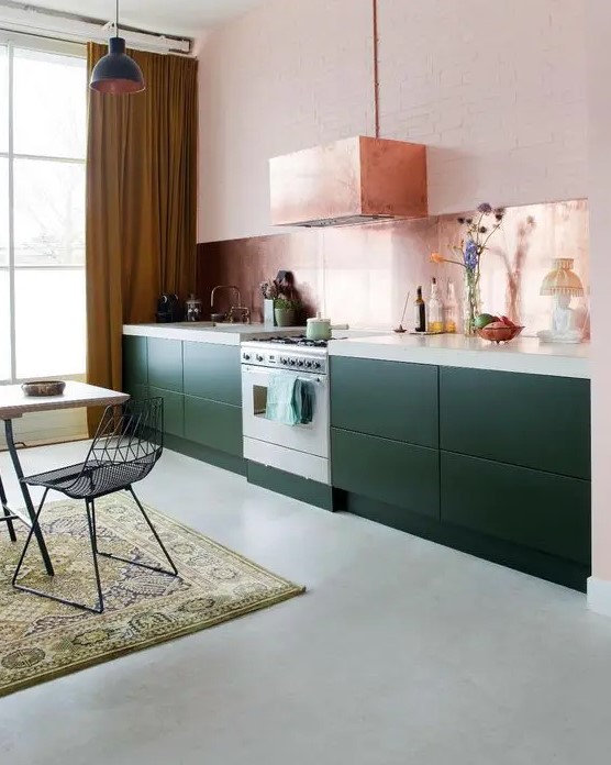 a pretty dark green one wall kitchen with a white stone countertop, a rose gold backsplash and a matching hood