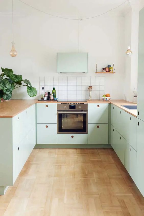 a pretty mint U-shaped kitchen with butcherblock countertops, a white square tile backsplash, pendant lamps and built-in appliances