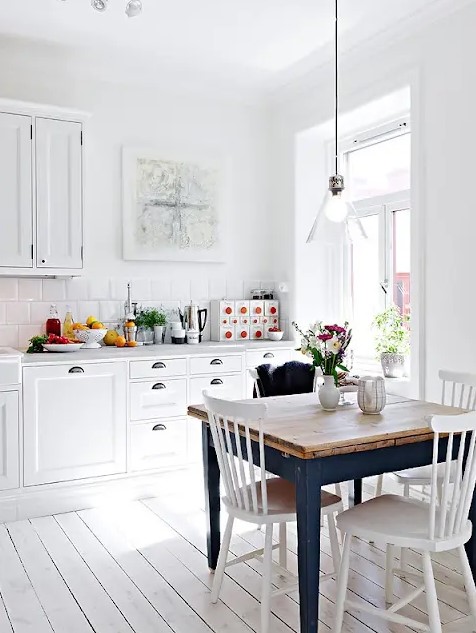 a pure white Scandinavian kitchen with retro cabinets, a glass pendant lamp and a vintage navy dining table