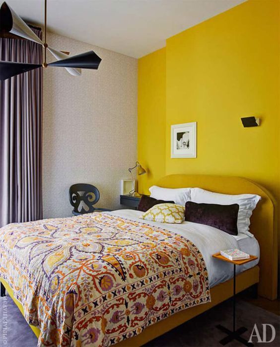 a refined mid-century modern bedroom with a yellow accent wall, whimsical furniture, printed bedding and a bold chandelier