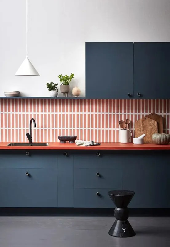 A refined navy one wall kitchen with an orange skinny tile backsplash plus an orange countertop and a white pendant lamp.