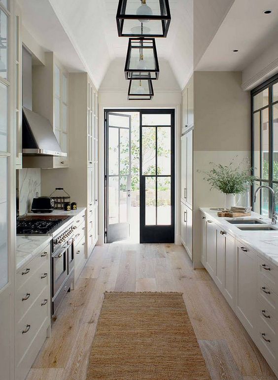 a refined white farmhouse kitchen with shaker cabients, black handles, a vintage style cooker and a hood, frame pendant lamps