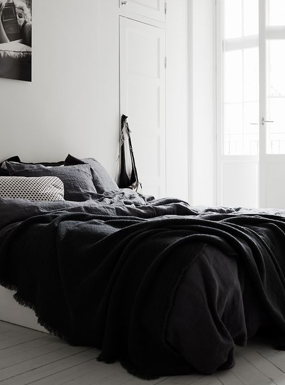 A relaxed Nordic bedroom with a bed with black bedding and a poster on the wall   who needs more for comfy sleeping