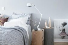a relaxed Scandinavian bedroom with a bed styled with grey and white bedding, stumps with a lamp and bottles and a printed rug