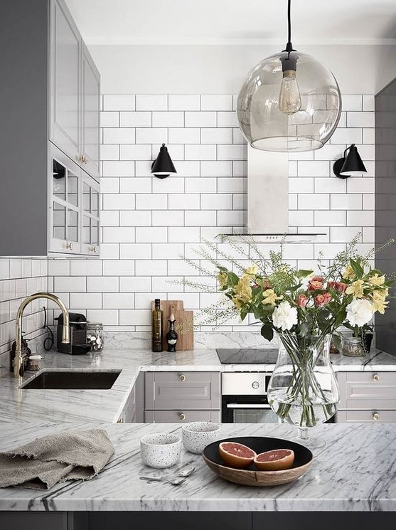 a retro-inspired Nordic kitchen with white tiles, stone countertops, grey cabinets and pendant lamps
