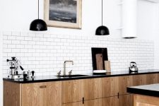 a retro-inspired Scandinavian kitchen with light wood cabinets, black countertops, black pendant lamps, a white tile backsplash
