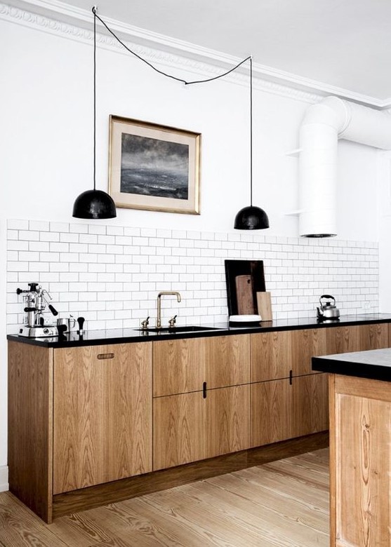A retro inspired Scandinavian kitchen with light wood cabinets, black countertops, black pendant lamps, a white tile backsplash