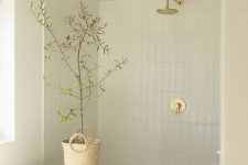 a serene Scandinavian bathroom clad with skinyn tiles, an oval tub, a sink, greenery in a basket, some neutral fixtures