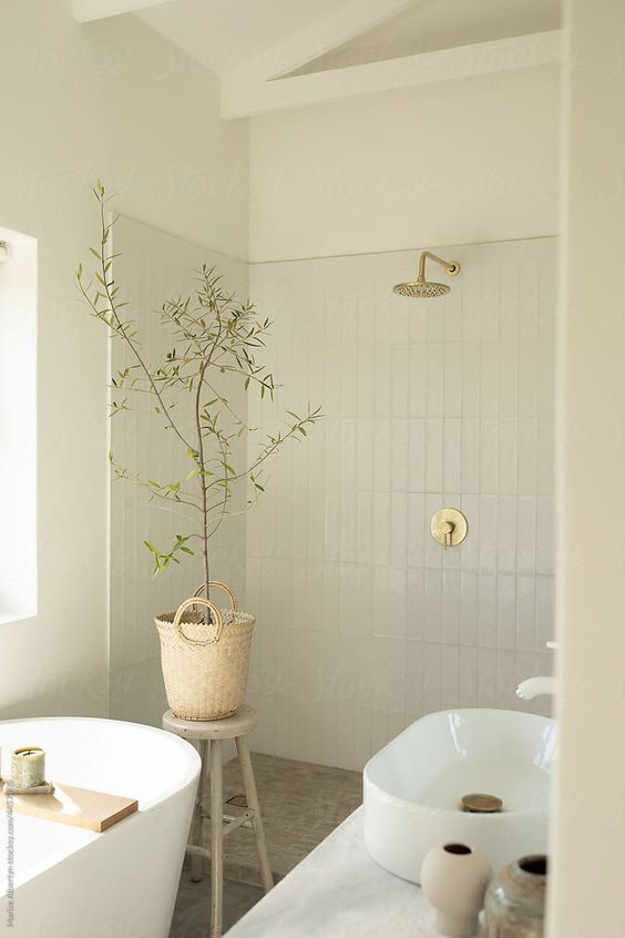 a serene Scandinavian bathroom clad with skinyn tiles, an oval tub, a sink, greenery in a basket, some neutral fixtures