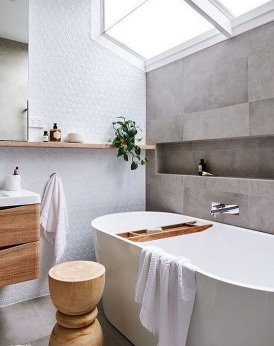 a serene Scandinavian bathroom with grey tiles, a white statement wall, much natural wood in decor and a skylight