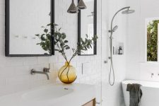 a serene Scandinavian bathroom with whiet subway tiles and penny ones, a stained vanity, a pendant lamp and a tub