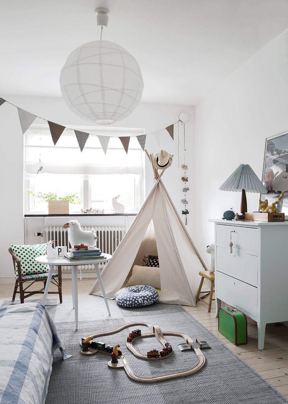 a serene Scandinavian kid’s room with a bunting, a teepee, a dresser, some wooden furniture, a bed and some cute toys