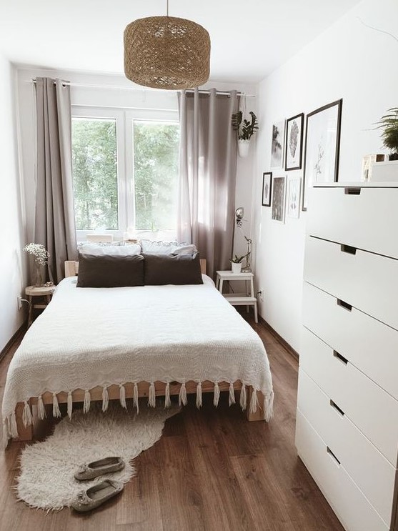 a simple and stylish small bedroom with a bed, mismatching nightstands, a dresser, a woven pendant lamp and grey curtains