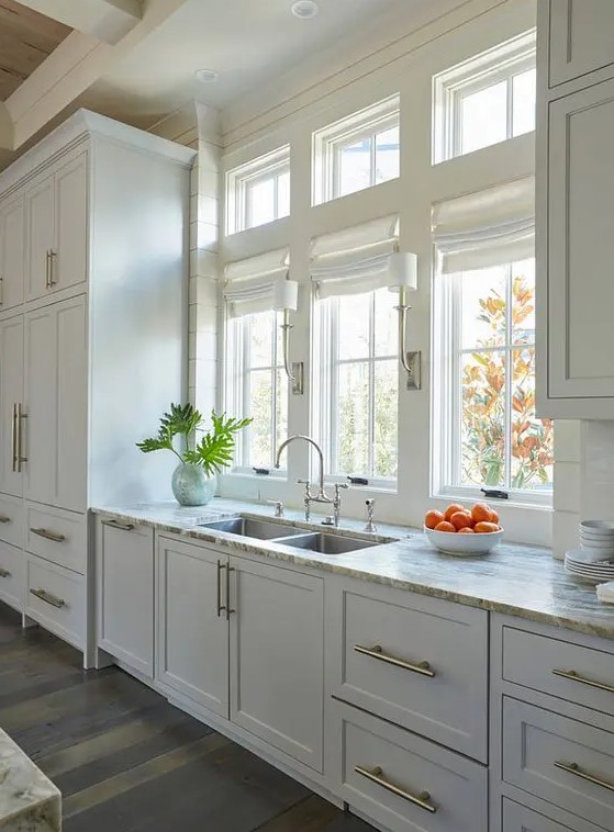 a simple white one wall kitchen with neutral stone countertops and gold handles is a beautiful and cool space