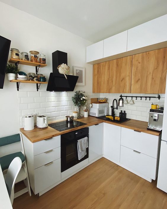 A small L shaped white kitchen with butcherblock countertops and MDF cabinets, a white subway tile backsplash and black appliances