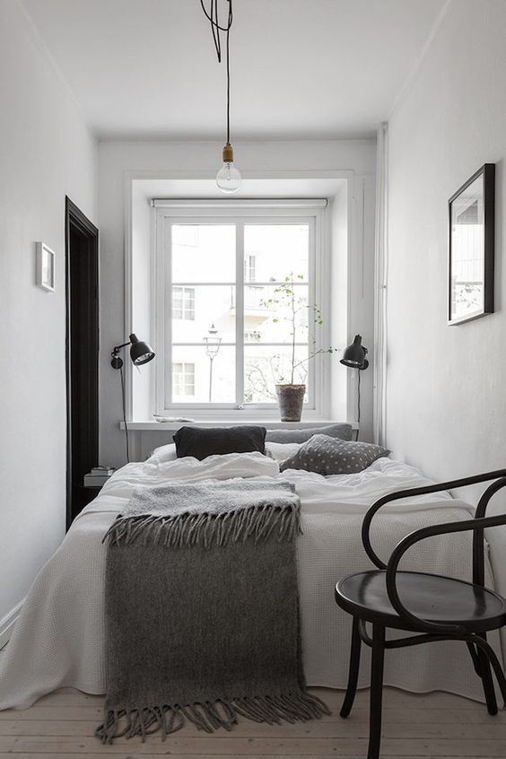 a small Nordic bedroom with only a bed and monochromatic bedding, black sconces and a black chair