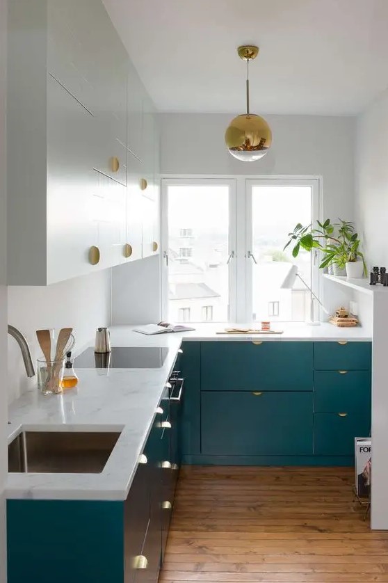 a small and chic tow-tone kitchen with gold handles and a gold pendant lamp plus potted greenery