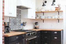 a small and cool black and white L-shaped kitchen with open shelves, butcherblock countertops, a printed tile backsplash and skylights